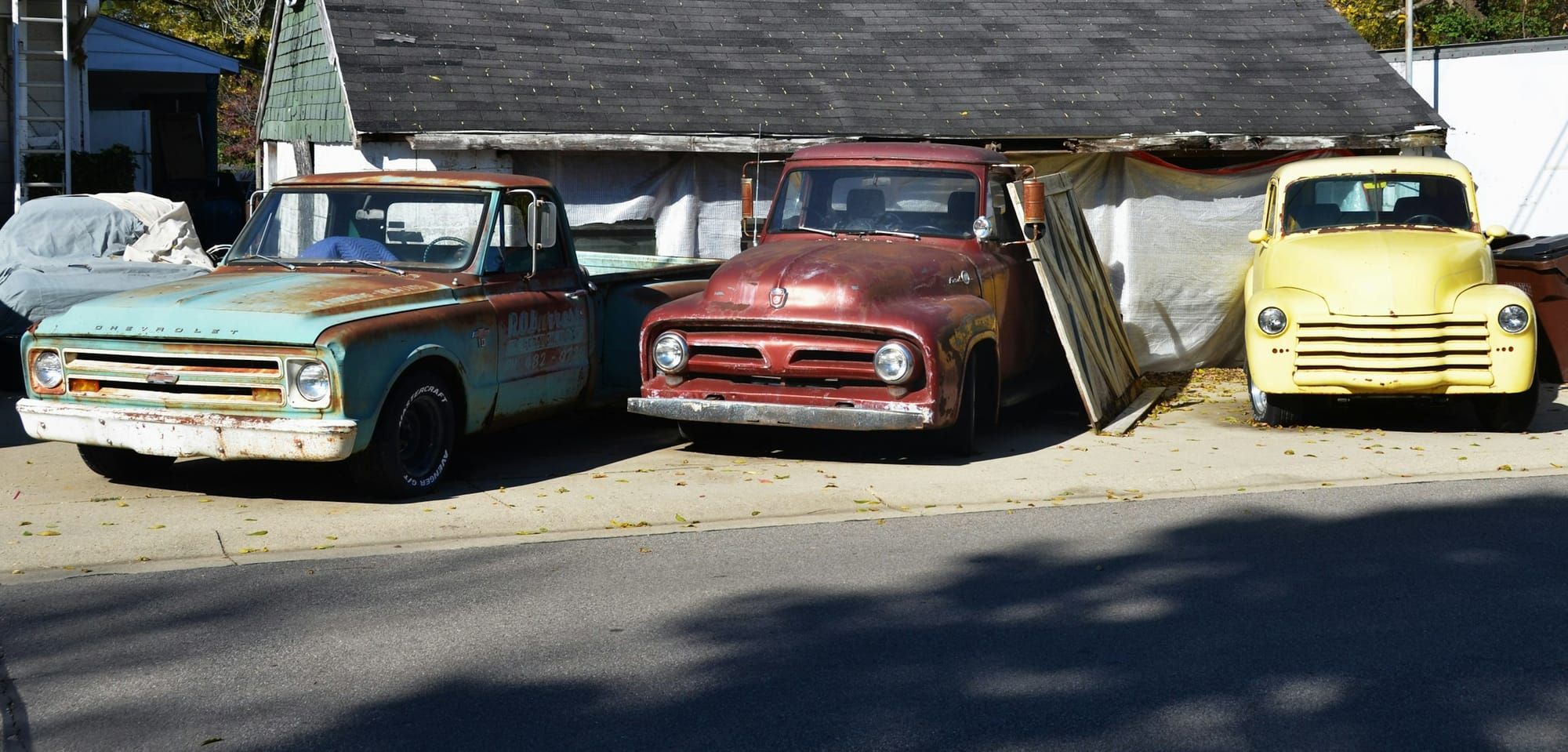 Three classic pickup trucks, a Chevrolet, a Ford, and a Chevrolet, parked in the sun